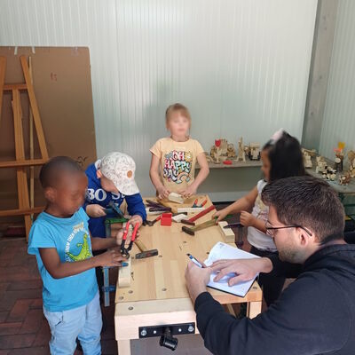 Das Bild zeigt den Tischler, wie er den Kindern an der Werkbank Hilfestellung gibt