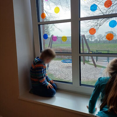 Das Bild zeigt zwei Kinder, die durch das Gruppenraumfenster schauen und etwas entdecken