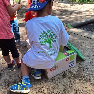 Das Bild zeigt einen sitzenden Jungen, der auf der Rückseite seines T-Shirts ein Kita Jübberde Emblem trägt