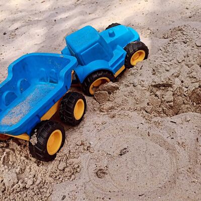 Das Bild zeigt einen blauen Spielzeugtrecker im Sandkasten mit Anhänger.