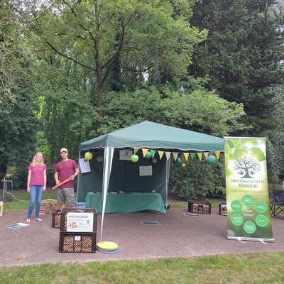 Auf dem Bild sieht man ein aufgebauten Stand mit vielen Kisten voller Holzbausteinen und zwei Kollegen vom Team der Kita Jübberde.