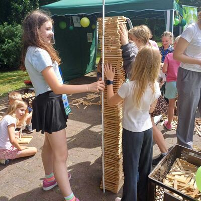 Das Bild zeigt zwei Mädchen im Vodergrund, die einen Holzstabturm bauen und vermessen.