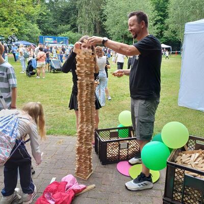 Das Bild zeigt Junge Jugendliche, die mit ihrem Vater zusammen einen hiohen Holzstabturm bauen.