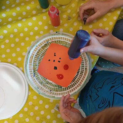 Das Bild zeigt, wie ein Kind mit buntem Papier, Farbe und einer Salatschleuder kreativ wird.