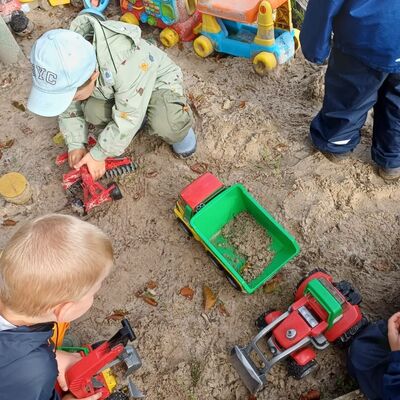 Das Bild zeigt spielende Kinder im Sandkasten mit Spieltreckern.