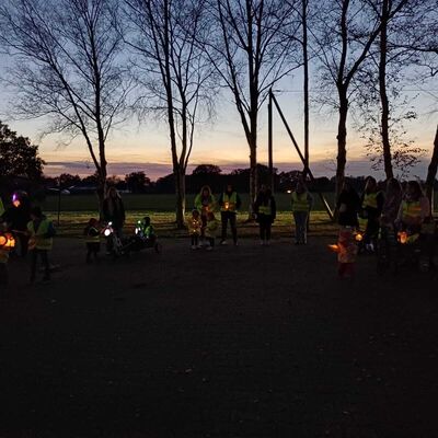Das Bild zeigt eine Gruppe von Kindern und Eltern, die zum Laternenlicht Lieder singen.