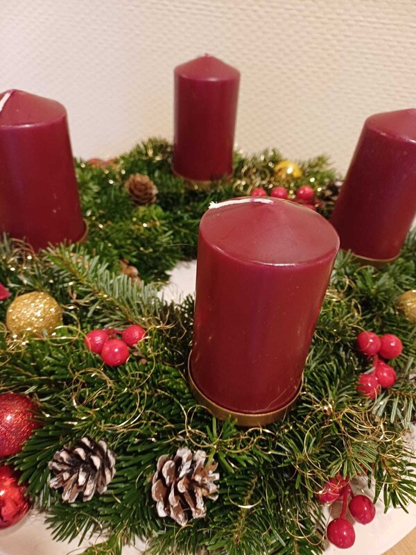 Bild vergr&ouml;&szlig;ern: Das Foto zeigt einen geschmückten Adventskranz mit roten Kerzen und Tannengrün.