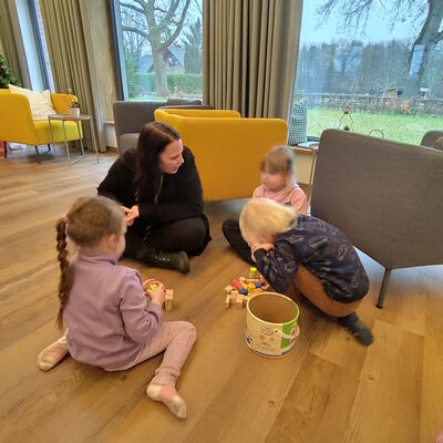 Das Foto zeigt eine Erzieherin, die mit drei spielenden Kindern in den Räumen der Upkamer ind Remels auf dem Boden sitzt und mitspielt.