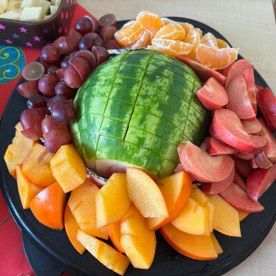 Das Foto zeigt hübsch arangiertes Obst auf einem Serviertelelr. Im Zentrum ist eine halbe Melone als Highlight für die Kinder.