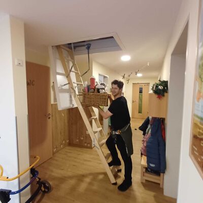 Das Foto zeigt einen Mitarbeiter der Kita Jübberde, der einen Weidenkorb voller mit Leckereien gefüllter Kinderstiefel vom Dachboden holt.